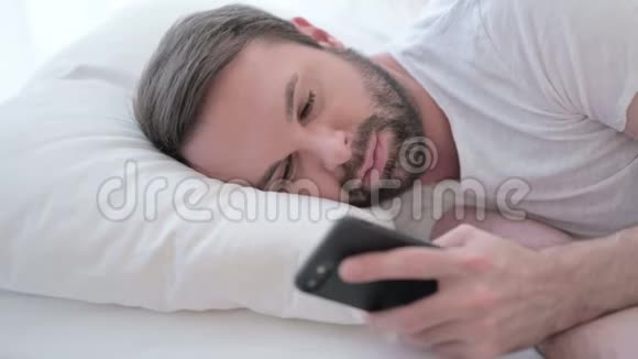 在床上使用智能手机关闭胡子青年视频的预览图