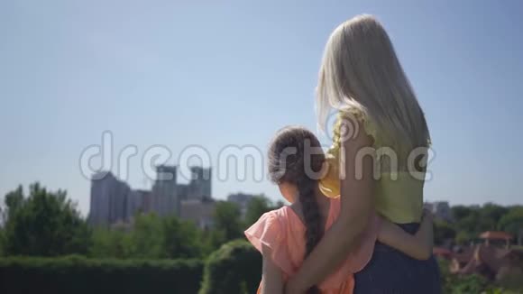 金发母亲和她的小女儿在夏天的花园或公园里休闲拥抱她妈妈的女孩幸福家庭视频的预览图