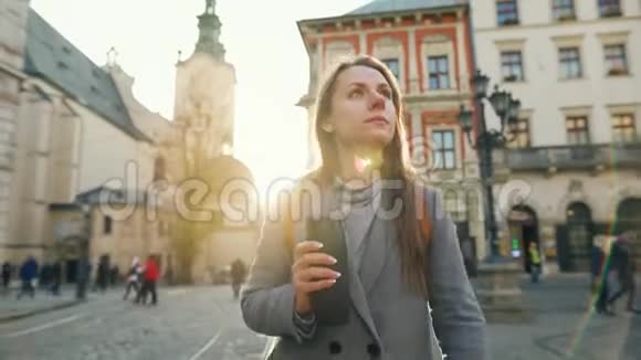 女人手里拿着一个保温杯走在街上看着她的手表匆忙地在日落时分参加一个会议视频的预览图