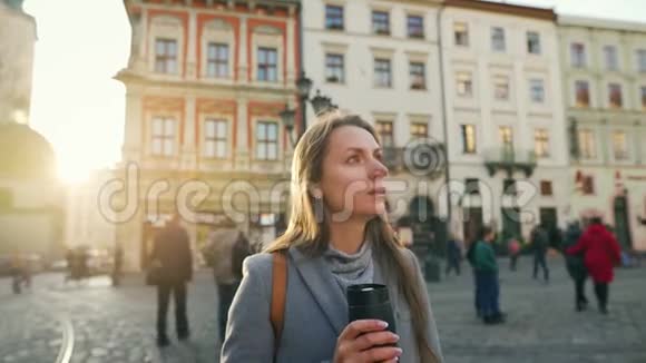 手里拿着保温杯的女人站在街中央看着她的手表等待着那个人视频的预览图