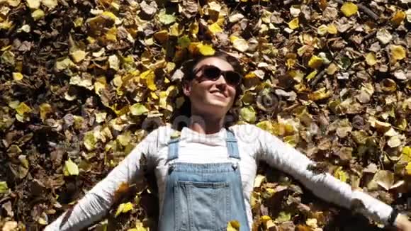 穿着牛仔布的年轻女人躺在秋黄的叶子上视频的预览图