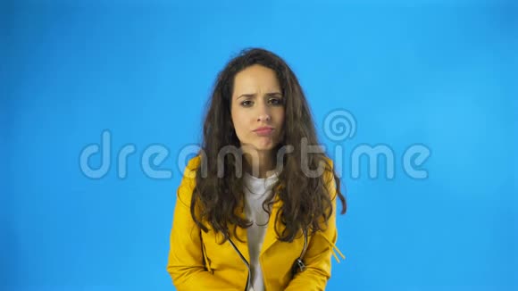 悲伤体贴年轻美丽的女人耸肩在工作室与蓝色背景视频的预览图