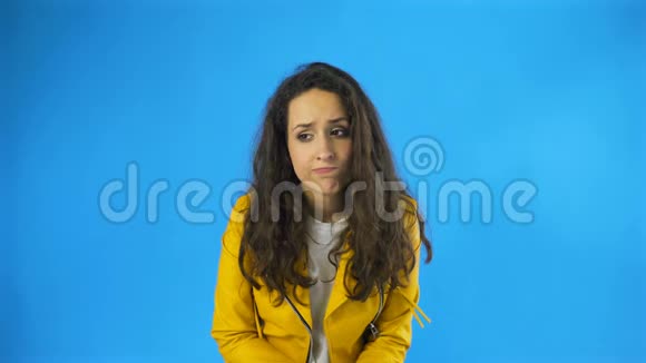 悲伤体贴年轻漂亮的女人穿着黄色夹克站在蓝底工作室视频的预览图