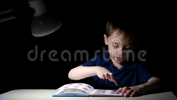 一个孩子喜欢晚上坐在一张灯点亮的桌子旁看书用手指指着书中的图画视频的预览图