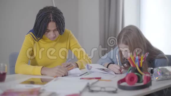 两个朋友一起在室内学习非裔美国人和白人女孩坐在桌子旁写作教育视频的预览图