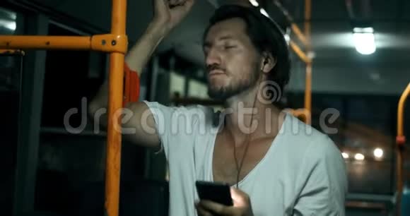 疲倦的人在公共汽车上听音乐睡觉他靠在扶手上有胡子的嬉皮士有问题视频的预览图