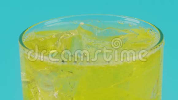 黄色软饮料在一个杯子与冰块在青色背景特写镜头视频的预览图