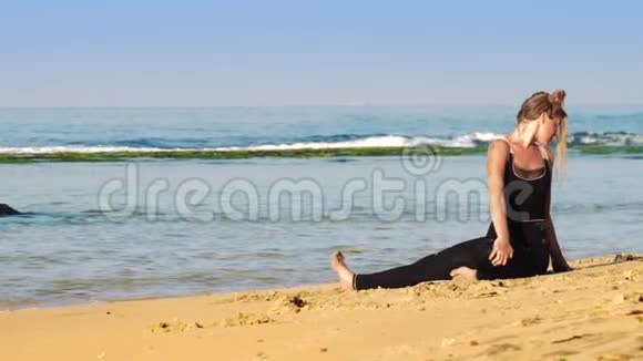 穿着黑色运动服的美女在金色沙滩上伸展视频的预览图