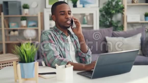 开朗的非裔美国人自由职业者使用手机和笔记本电脑在家工作做远距离工作视频的预览图