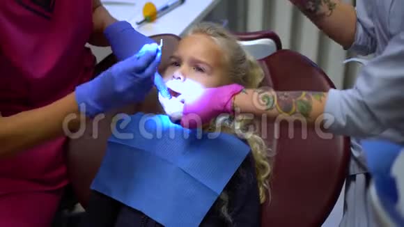 牙医和她的助手用纹身的手修复小女孩的牙齿视频的预览图