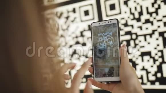 一位使用智能手机的女士在一个现代化公园的凉亭互动墙上扫描大型QR码视频的预览图