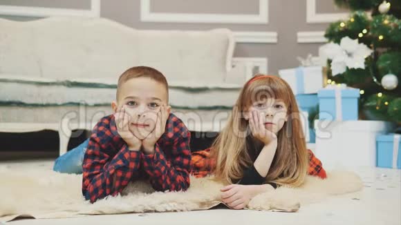 喜气洋洋的弟弟和妹妹正穿着红格子的衣服躺在毛毯上等待新年的到来视频的预览图