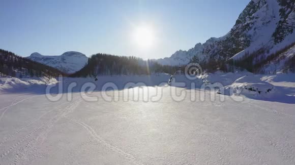 在阳光明媚的冬日在山谷上覆盖着雪的冰湖上空飞行欧洲阿尔卑斯山脉户外爱好者视频的预览图