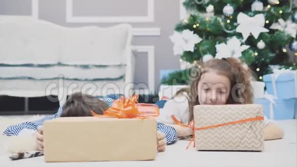 微笑着的兄弟姐妹们享受着圣诞节的时光躺在枞树下的地毯上从两个后面露出头来视频的预览图