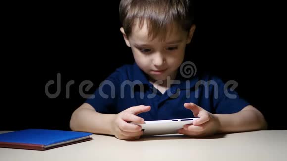 一个快乐的孩子在晚上用智能手机快乐地看着一幅漫画微笑着视频的预览图