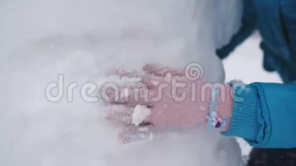 手套里女孩的特写在冬天的街道上雕刻一个雪人视频的预览图
