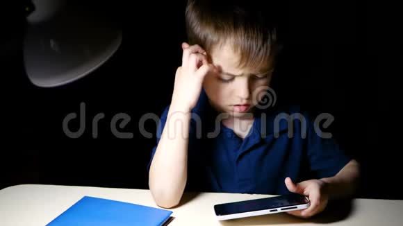 一个孩子坐在家里的桌子旁晚上用智能手机沉思地看着一幅漫画视频的预览图