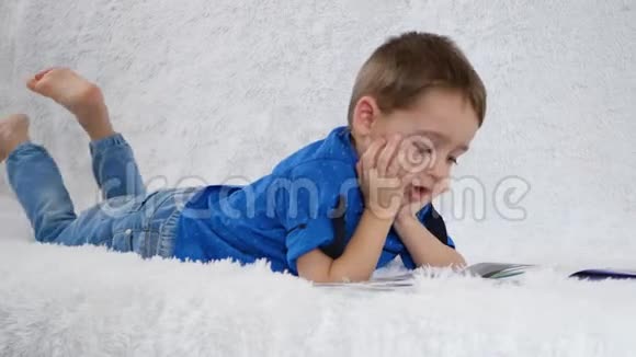 一个快乐的孩子快乐地读着一本躺在白色沙发上的书儿童发展的概念视频的预览图