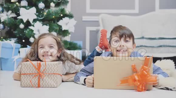 漫不经心微笑着的小兄弟姐妹享受着圣诞节的时光和礼物躺在杉树下的地毯上视频的预览图
