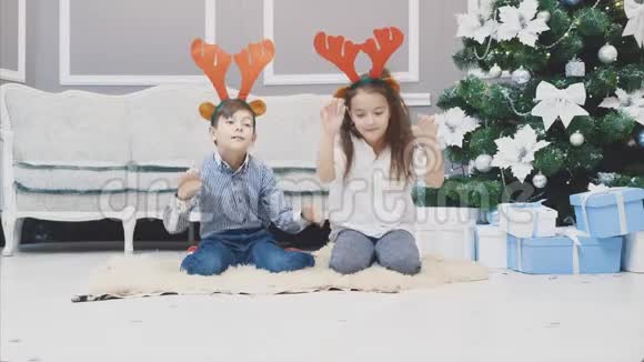 穿着红驯鹿鹿角的可爱的孩子完全精疲力竭在圣诞树附近的地毯上睡着了而不是视频的预览图