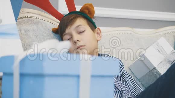 特写视频小男孩头上有驯鹿鹿角睡在沙发上圣诞老人模糊的视频的预览图