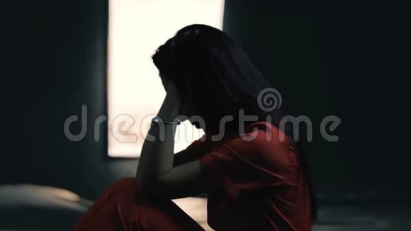 心碎的女人独自在窗户里哭泣忧郁沮丧的女人坐在黑暗的走廊上的剪影视频的预览图