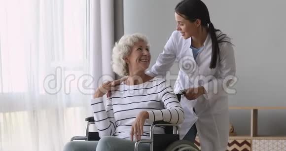 一位年轻的女护士员在轮椅上帮助年迈的祖母视频的预览图