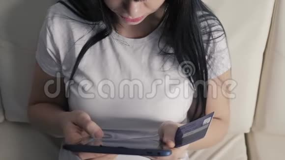 女孩用笔记本电脑数字平板电脑制作网上销售购物概念黑发女人躺在沙发上看着网上支付的商店视频的预览图