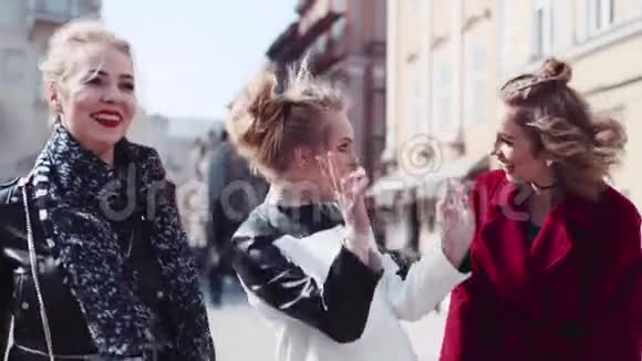快乐的三个朋友在老市中心徘徊笑着开玩笑穿红色外套的女人拥抱她的朋友视频的预览图
