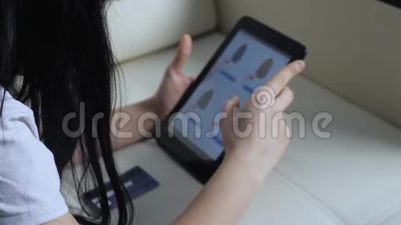 女孩用数字平板电脑制作网上购物概念黑发女人躺在沙发上看着网上商店付钱视频的预览图