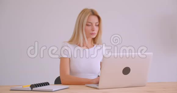 一位成年白种人金发女商人用笔记本电脑在办公室里看着照相机的特写照片视频的预览图