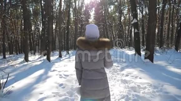 在阳光明媚的冬天森林里散步的年轻女子的后景无法辨认的女孩在雪地里漫步视频的预览图