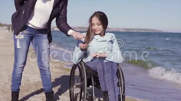 坐在轮椅上的年轻残疾妇女和她的母亲在海边的沙滩上玩跳石游戏视频的预览图