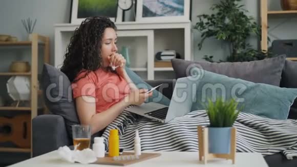 不健康的女孩在网上用显示体温计和药丸的笔记本电脑与医生交谈视频的预览图