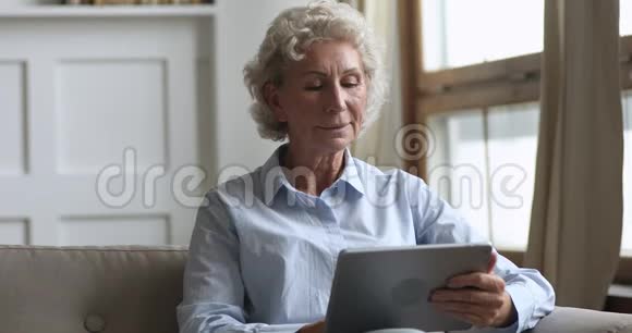 幸福的老妇人拿着数码平板电脑在沙发上放松视频的预览图
