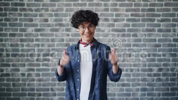 戴眼镜的快乐深色头发的人在砖背景上竖起大拇指视频的预览图