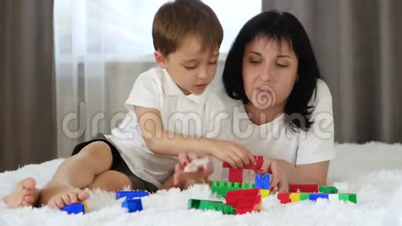 幸福的家庭躺在床上休息母婴游戏搭建彩色积木妈妈吻她的孩子视频的预览图