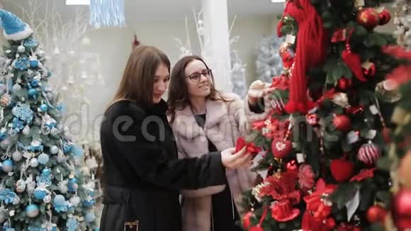 商场里有两个女人在考虑新年装饰挂在销售区的人造树上视频的预览图