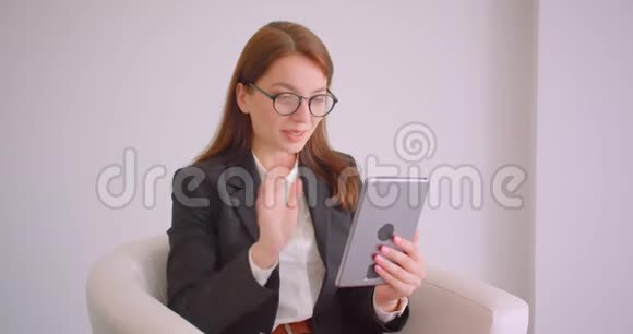一位戴眼镜的年轻白种人女商人的特写肖像他在平板电脑上打着一个视频电话坐在平板电脑里打招呼视频的预览图