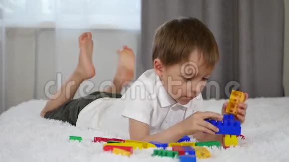 一个可爱的小男孩躺在床上玩彩色积木儿童从meccano建设视频的预览图