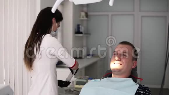 Brunette女牙医从背部站立为男性病人在口腔科接受牙科治疗做准备视频的预览图
