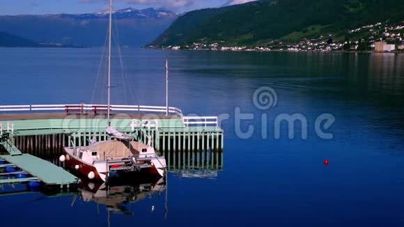 木船双体帆船系在挪威峡湾平静的水面上浅绿色的码头岩石上视频的预览图