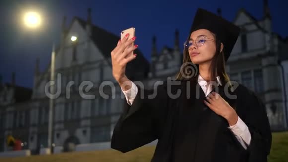 可爱的毕业生女孩用她的手机做准备视频的预览图