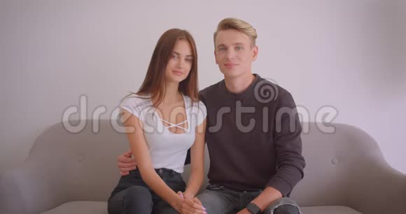 一对年轻可爱的白种人夫妇的特写镜头他们看着镜头开心地坐在室内的沙发上视频的预览图
