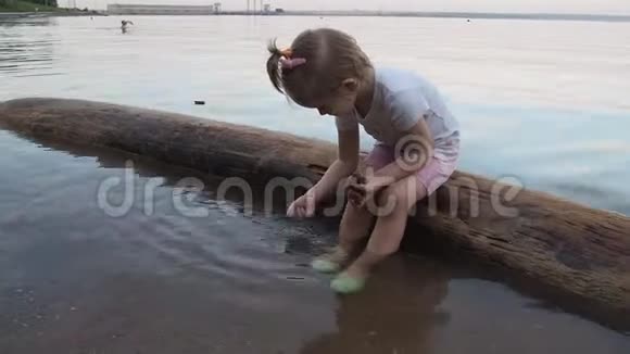 一个小女孩在海上玩手里拿着鹅卵石她坐在木头上洗石头晚上关门视频的预览图