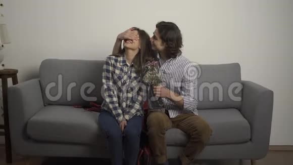 一个微笑的男人用手捂住女朋友的眼睛在客厅里呈现花束视频的预览图
