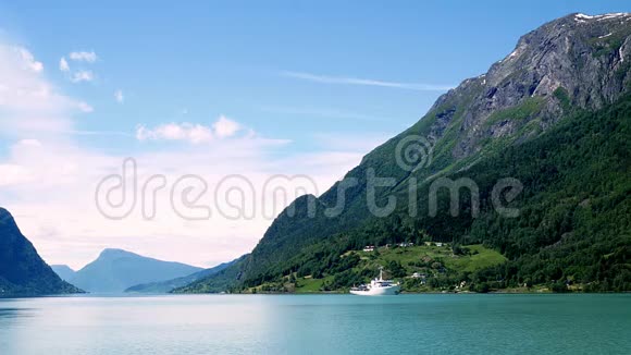 在阳光明媚的日子里白色游艇在挪威的峡湾上航行背景是群山和蓝天白云视频的预览图