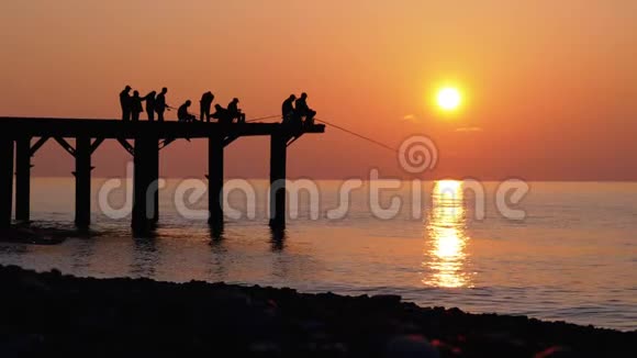 渔夫的剪影与钓竿在海上日落坐在码头上慢动作视频的预览图