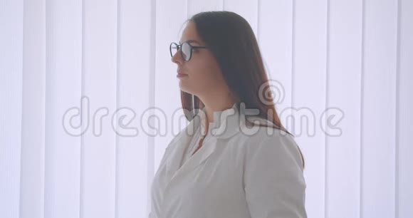 年轻的白种人女医生戴着眼镜穿着白大褂看着站在室内的摄像机特写照片视频的预览图