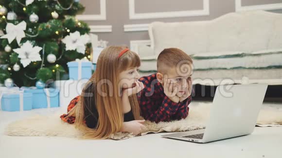 温暖的4k视频美丽的兄弟姐妹看新年电影同时躺在地毯下圣诞杉木视频的预览图